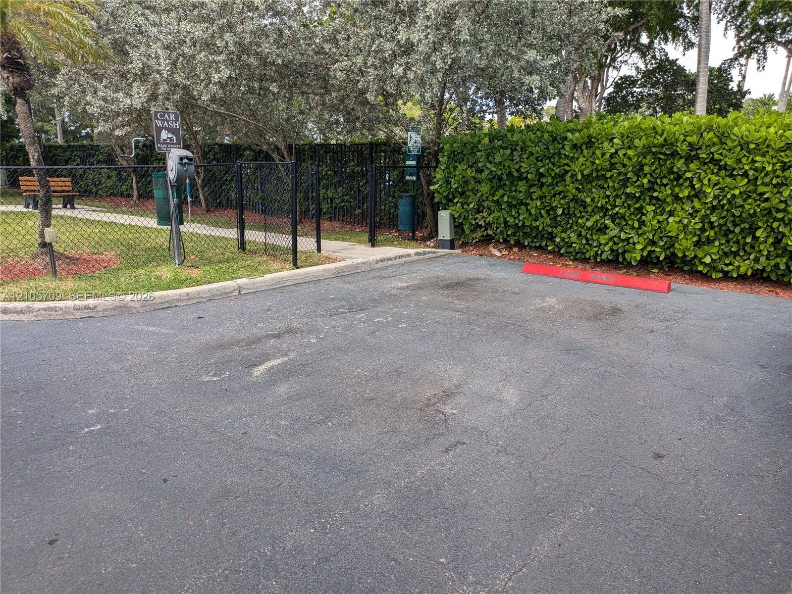 300 Three Islands Boulevard, #516, Hallandale Beach, FL 33009 Paved parking area featuring a dedicated car wash station, chain-link perimeter fencing, and mature hedge landscaping
