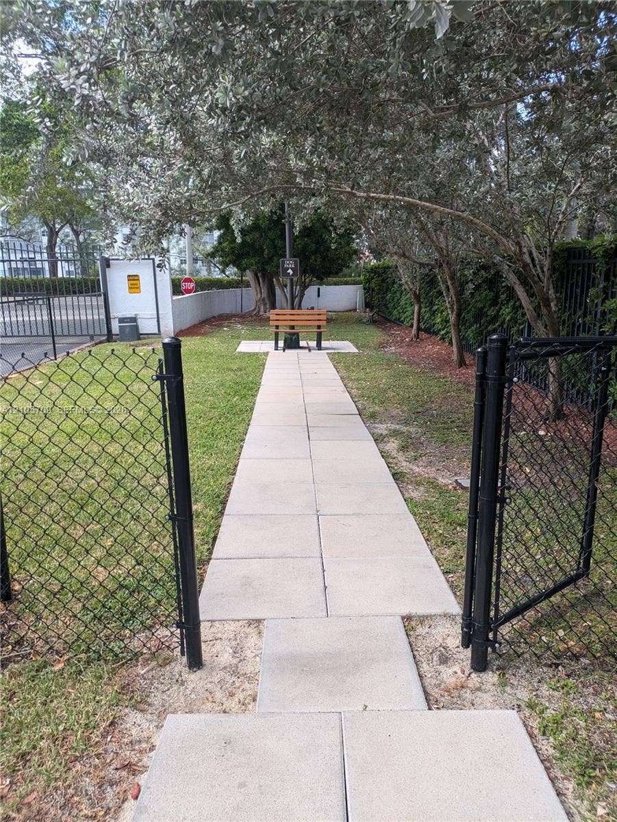 300 Three Islands Boulevard, #516, Hallandale Beach, FL 33009 Fenced outdoor space featuring a paved walkway, mature trees, and a permanent wooden bench