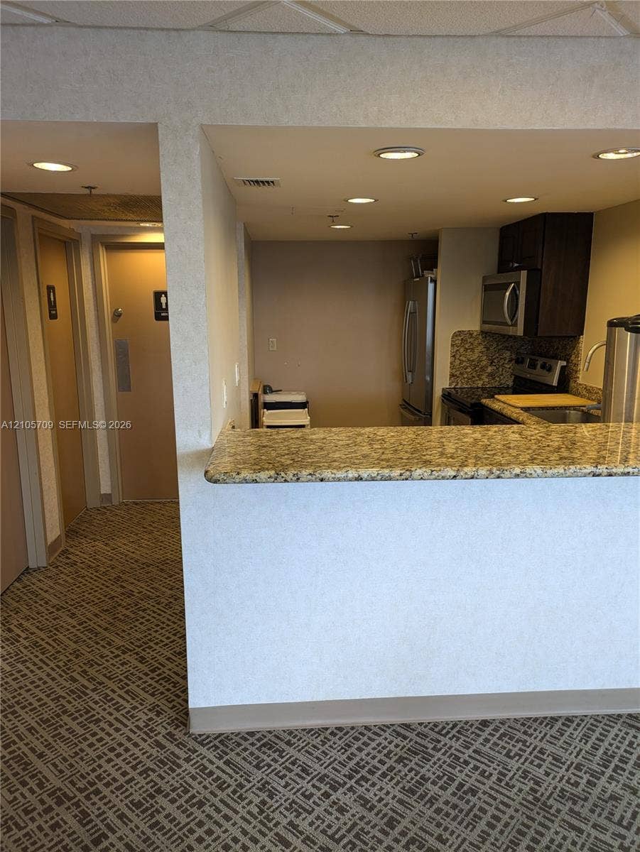 300 Three Islands Boulevard, #516, Hallandale Beach, FL 33009 Kitchen featuring a stone-look countertop breakfast bar, recessed ceiling lighting, dark cabinetry, and integrated stainless steel appliances