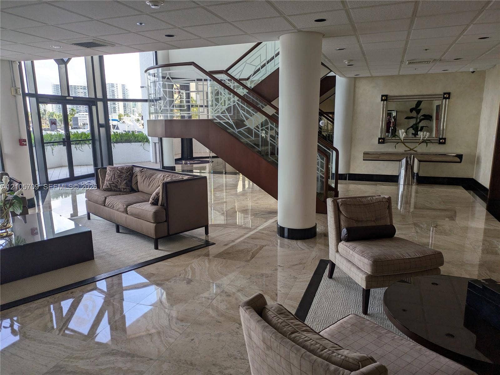 300 Three Islands Boulevard, #516, Hallandale Beach, FL 33009 Polished stone flooring, floor-to-ceiling glass paneling, and an open staircase featuring metal railing with geometric detailing