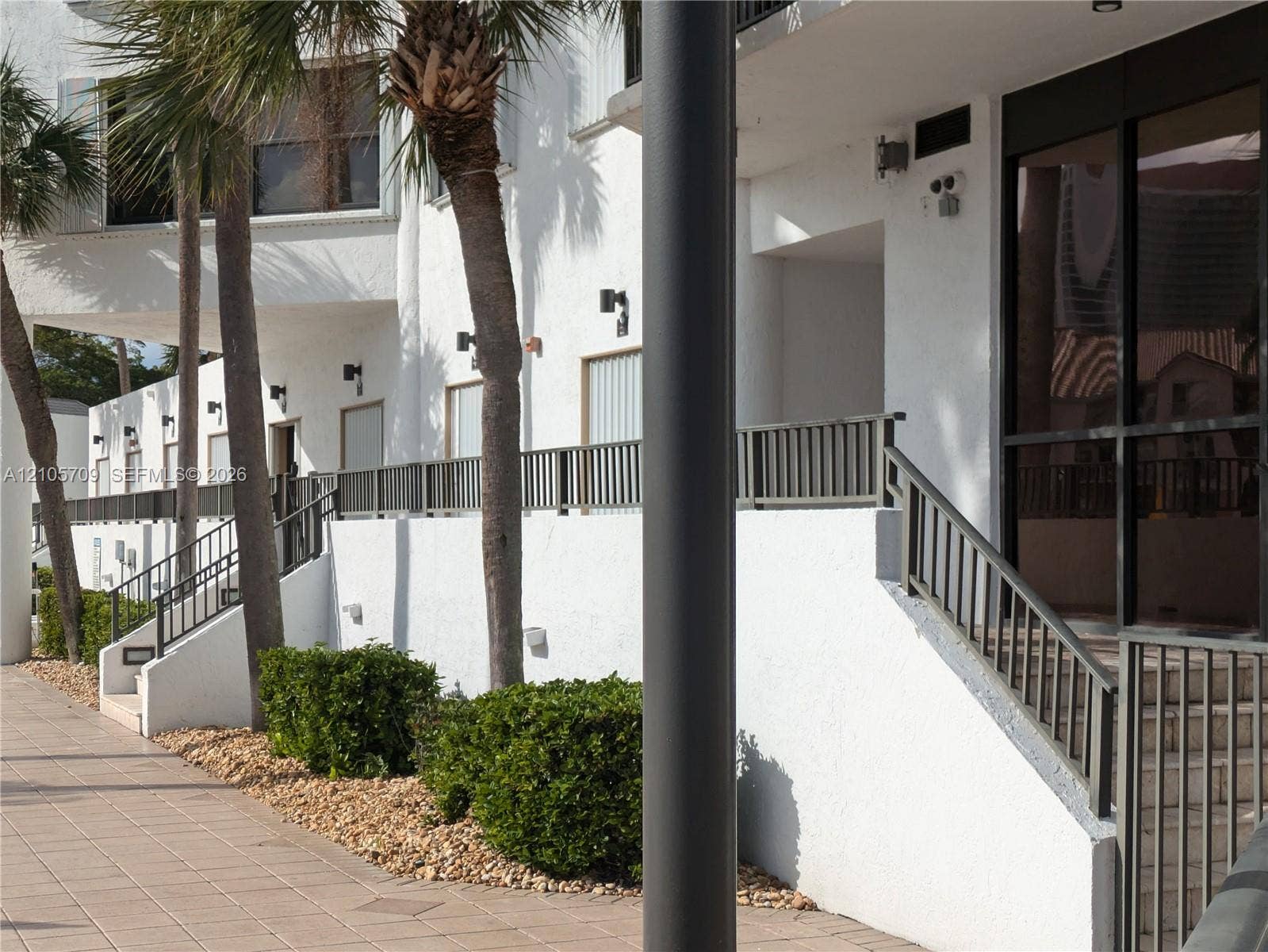 300 Three Islands Boulevard, #516, Hallandale Beach, FL 33009 Stucco exterior featuring metal railings, uniform wall-mounted lighting, and paved ground-level walkways with landscaped shrubbery