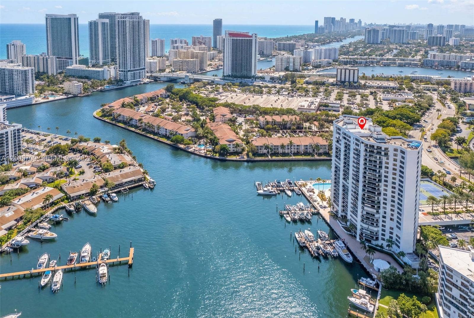 300 Three Islands Boulevard, #516, Hallandale Beach, FL 33009 High-rise building situated on a waterway, featuring private boat slips, an outdoor swimming pool, and a tennis court
