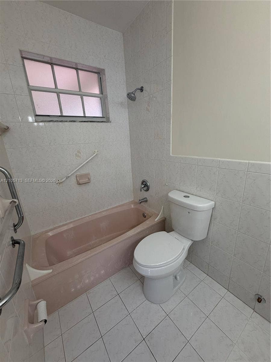 Bathroom featuring full-height wall tiling, white ceramic tile flooring, a built-in tub, and a multi-pane window