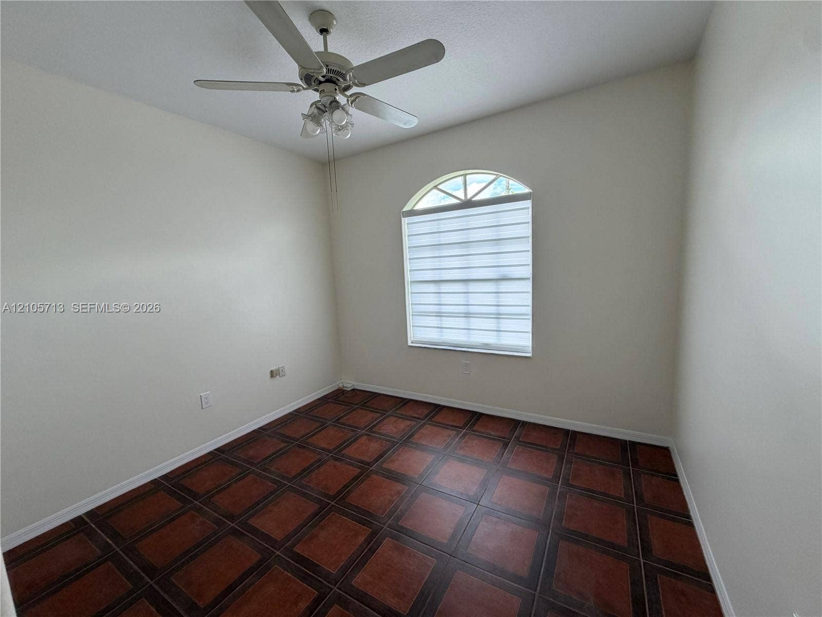 Room featuring terra cotta-style tile flooring, an arched window with integrated mullions, and a central ceiling fan with multi-light fixture