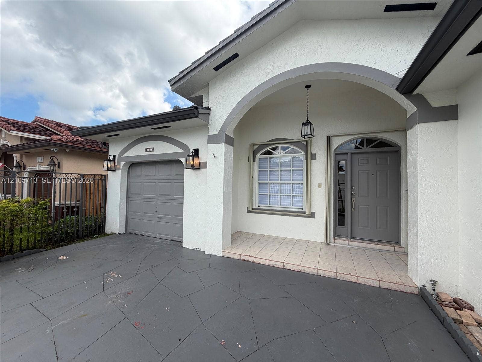 Stucco exterior featuring a covered entryway with a stone-style arch, a tiled front porch, a multi-pane window with arched transom, and a paneled entry door with sidelights