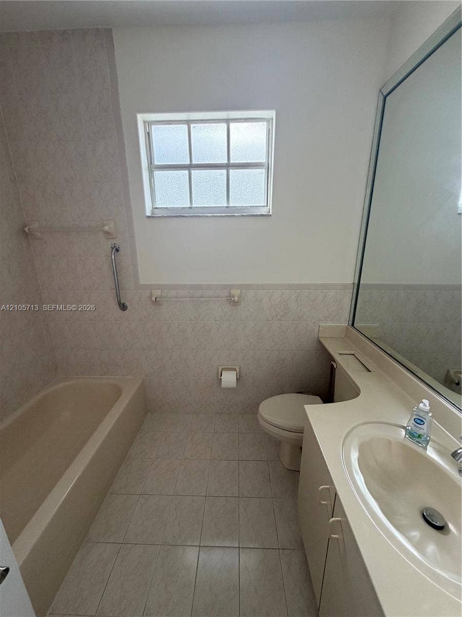 Bathroom featuring a solid-surface integrated vanity countertop, large wall-mounted mirror, ceramic tile flooring, and a window with a paneled design