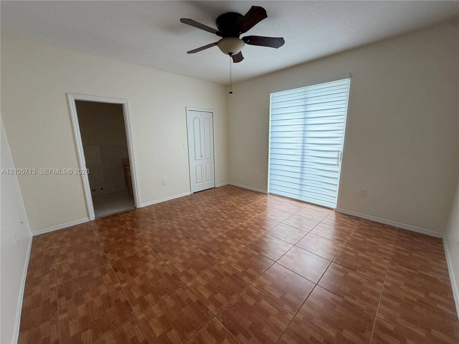 Room featuring tile flooring, a ceiling fan with integrated lighting, a sliding glass door with horizontal blinds, and a built-in closet with double doors