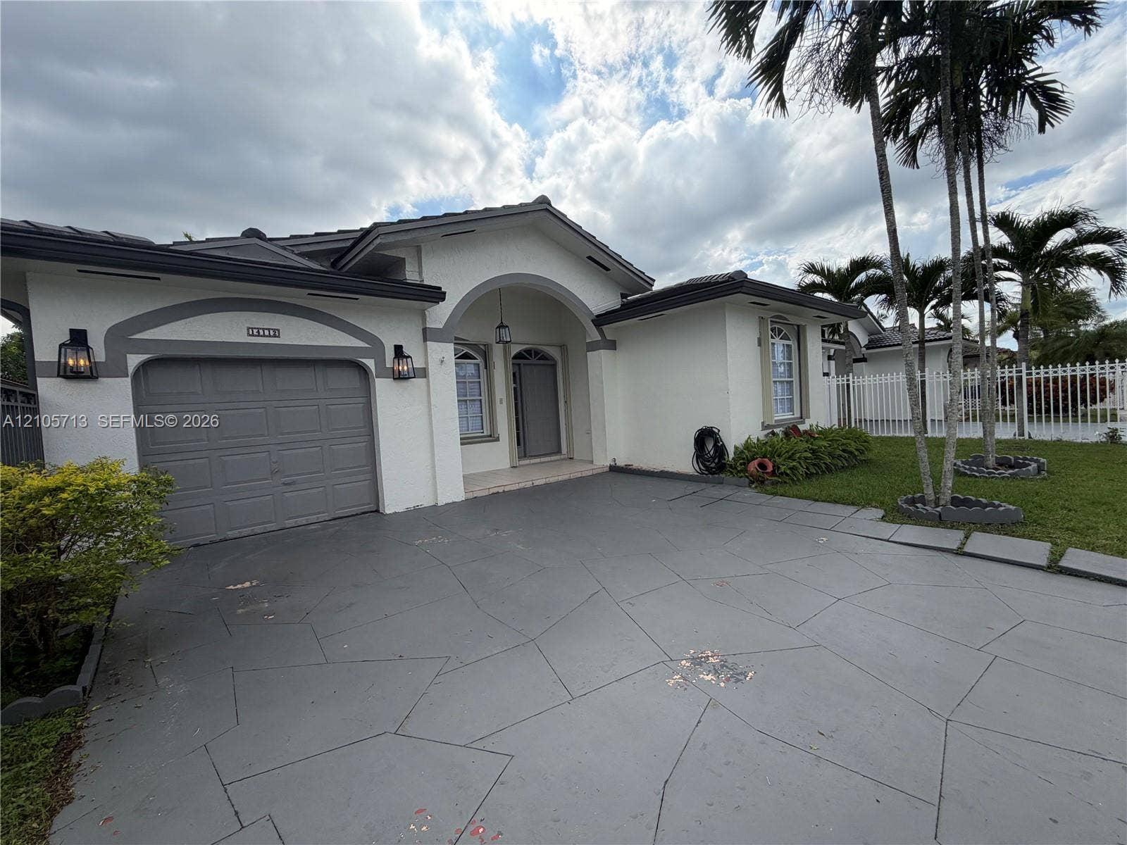 Stucco exterior with arched entryway, patterned concrete driveway, and attached garage featuring exterior wall-mounted lanterns