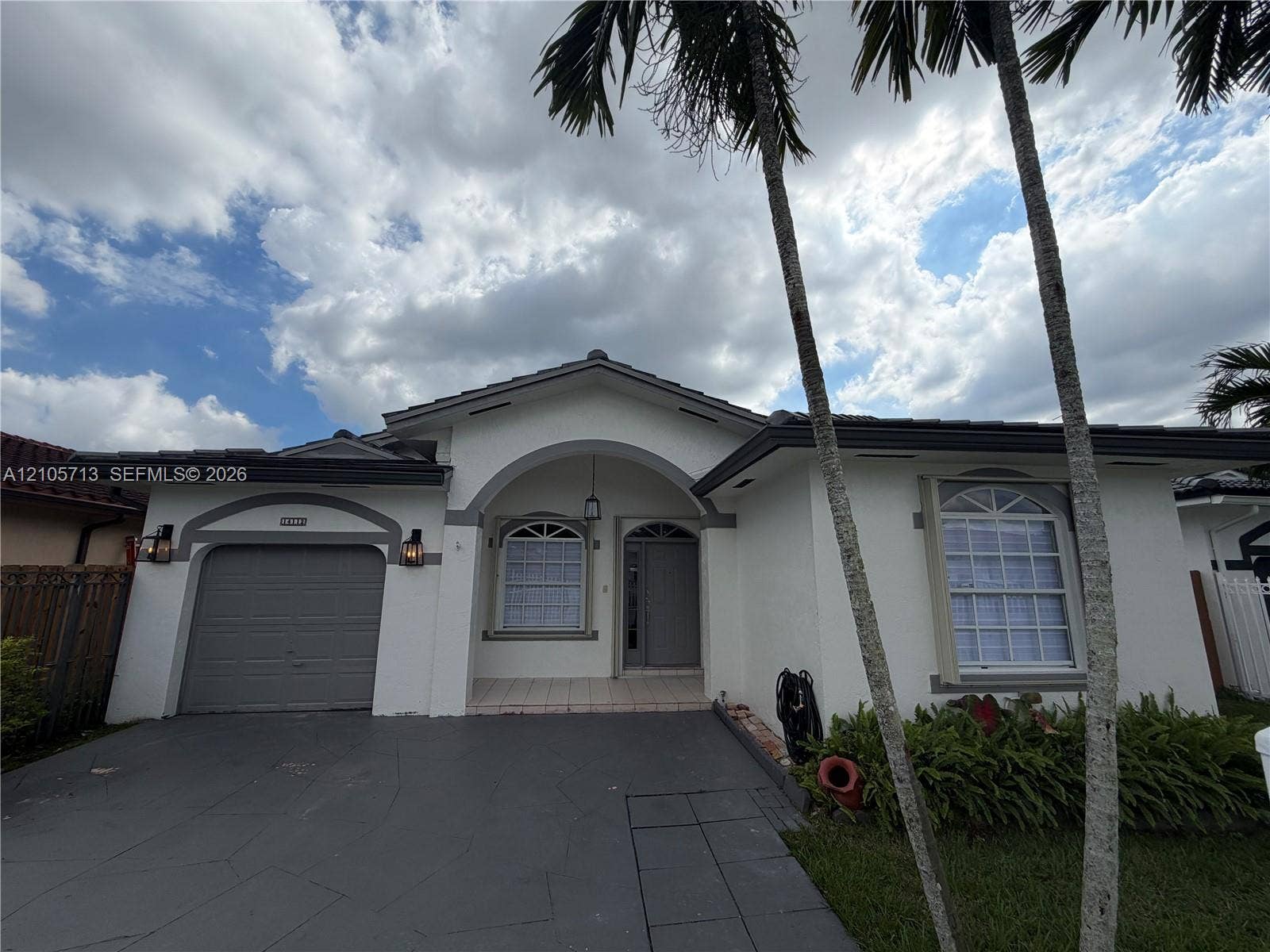 Single-story stucco exterior featuring a tiled roof, arched entryway, arched window accents, and a paved driveway