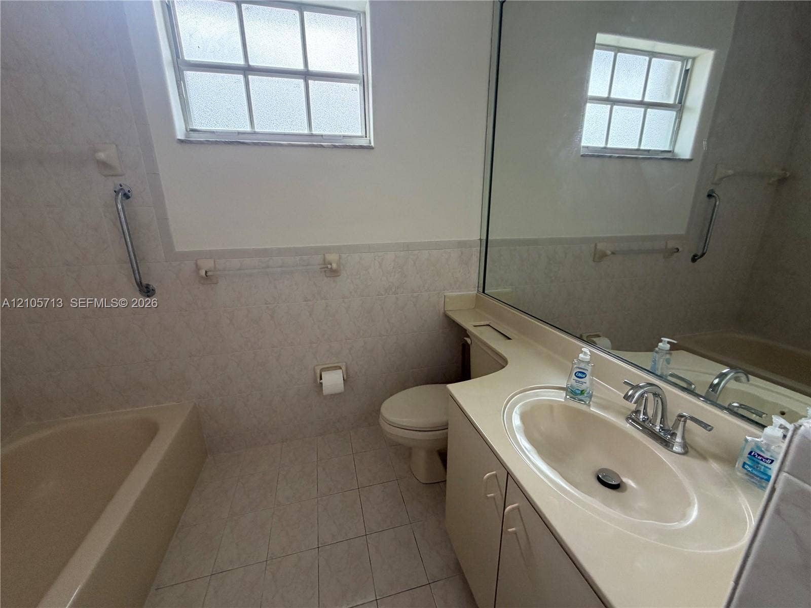 Bathroom featuring ceramic tile flooring, tub-shower combination, integrated vanity countertop with sink, wall-spanning vanity mirror, and multi-pane window