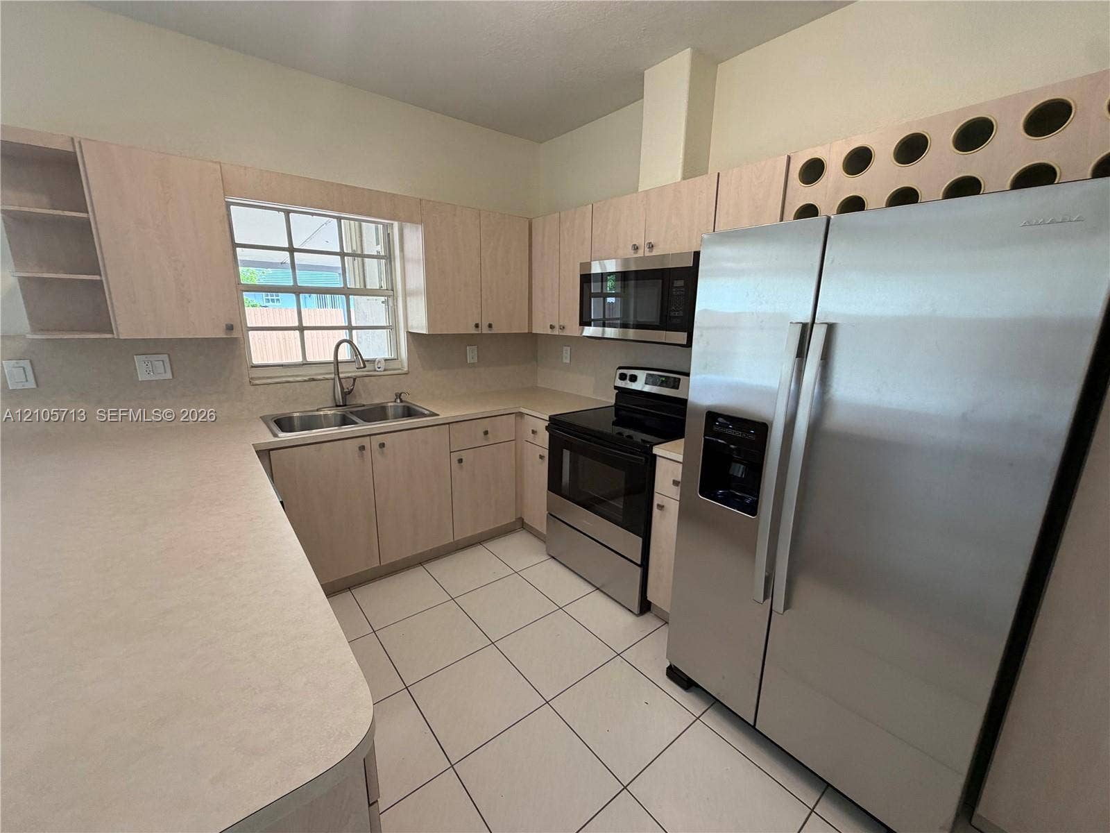 Kitchen featuring light-finish cabinetry, built-in wine rack storage, stainless steel appliances, double-basin sink, and tile flooring