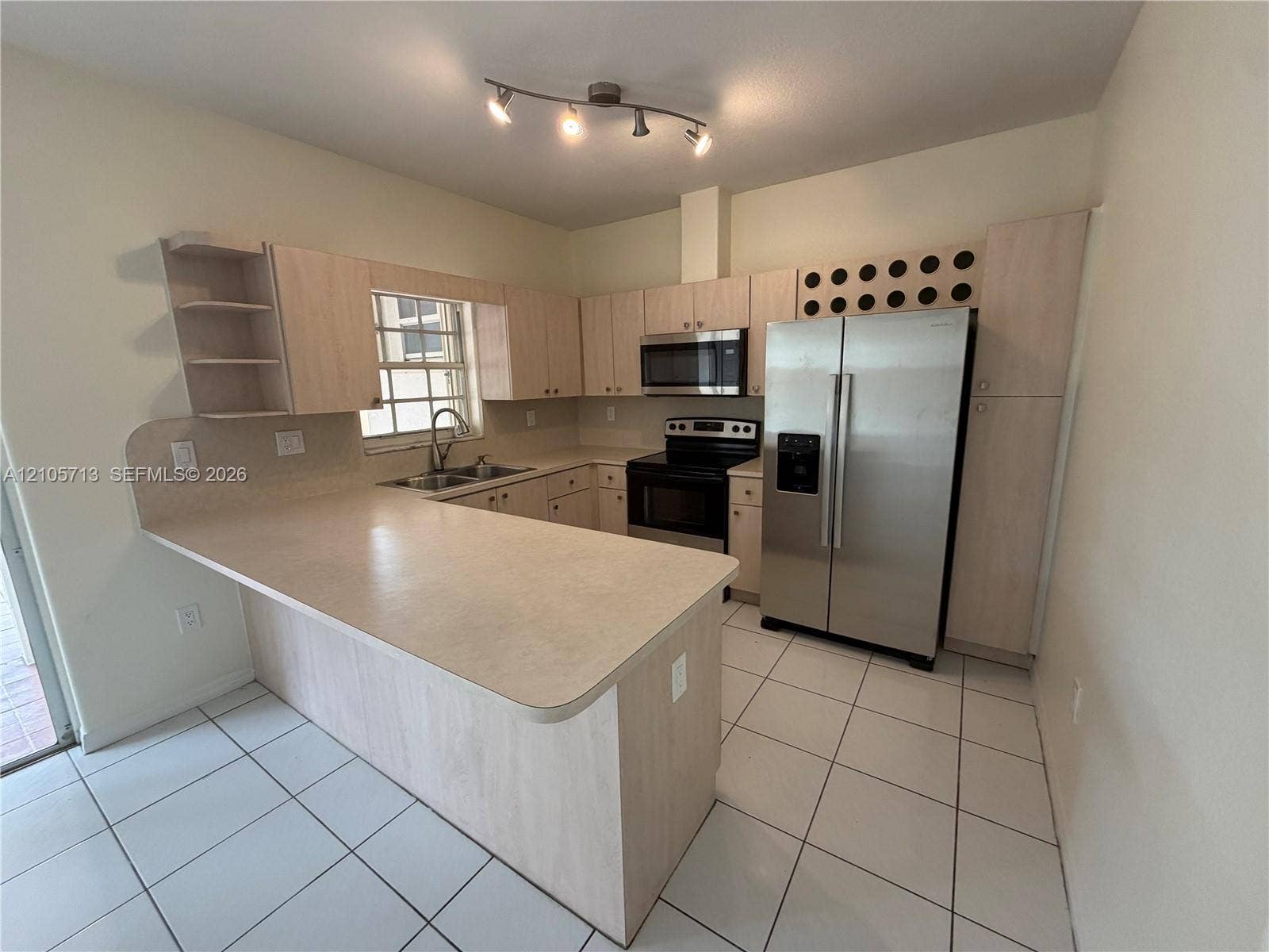Kitchen featuring light-finish cabinetry, neutral solid-surface countertops, tile flooring, integrated wine storage, and stainless steel appliances
