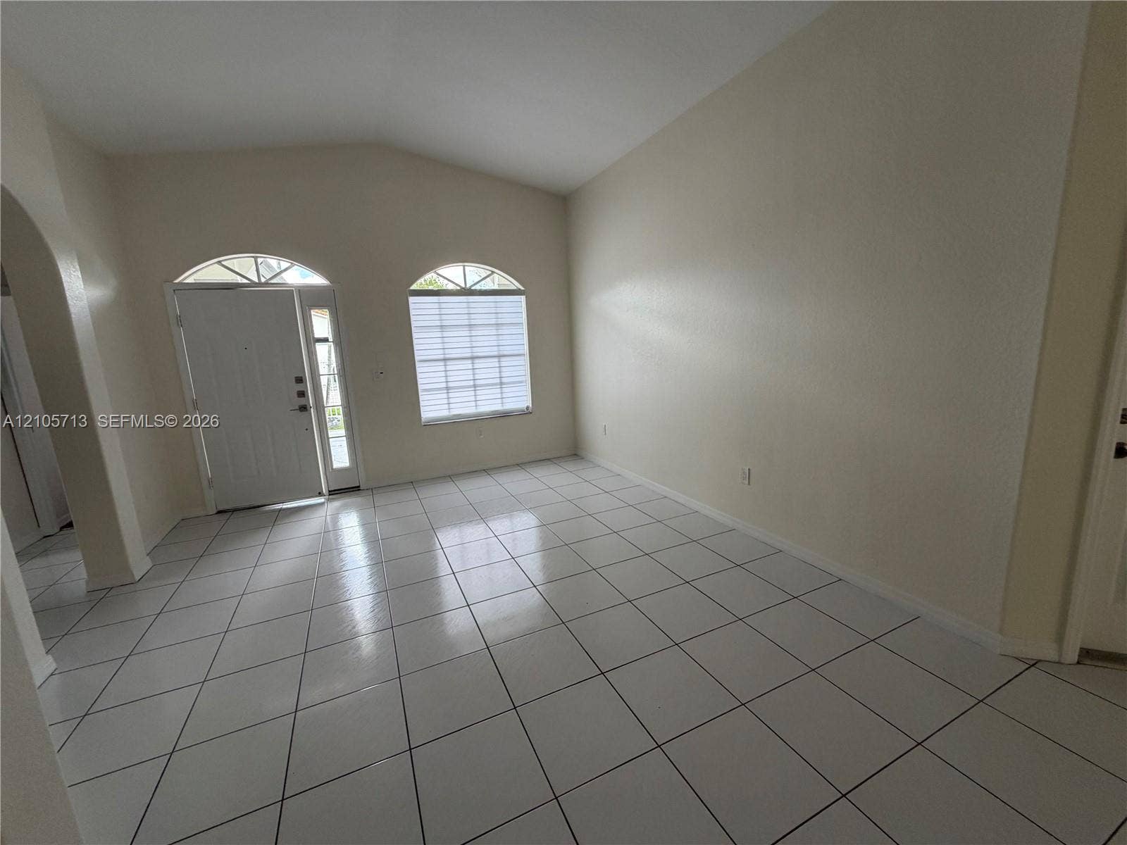 Vaulted ceilings, white ceramic tile flooring, arched window detailing, and neutral wall tones