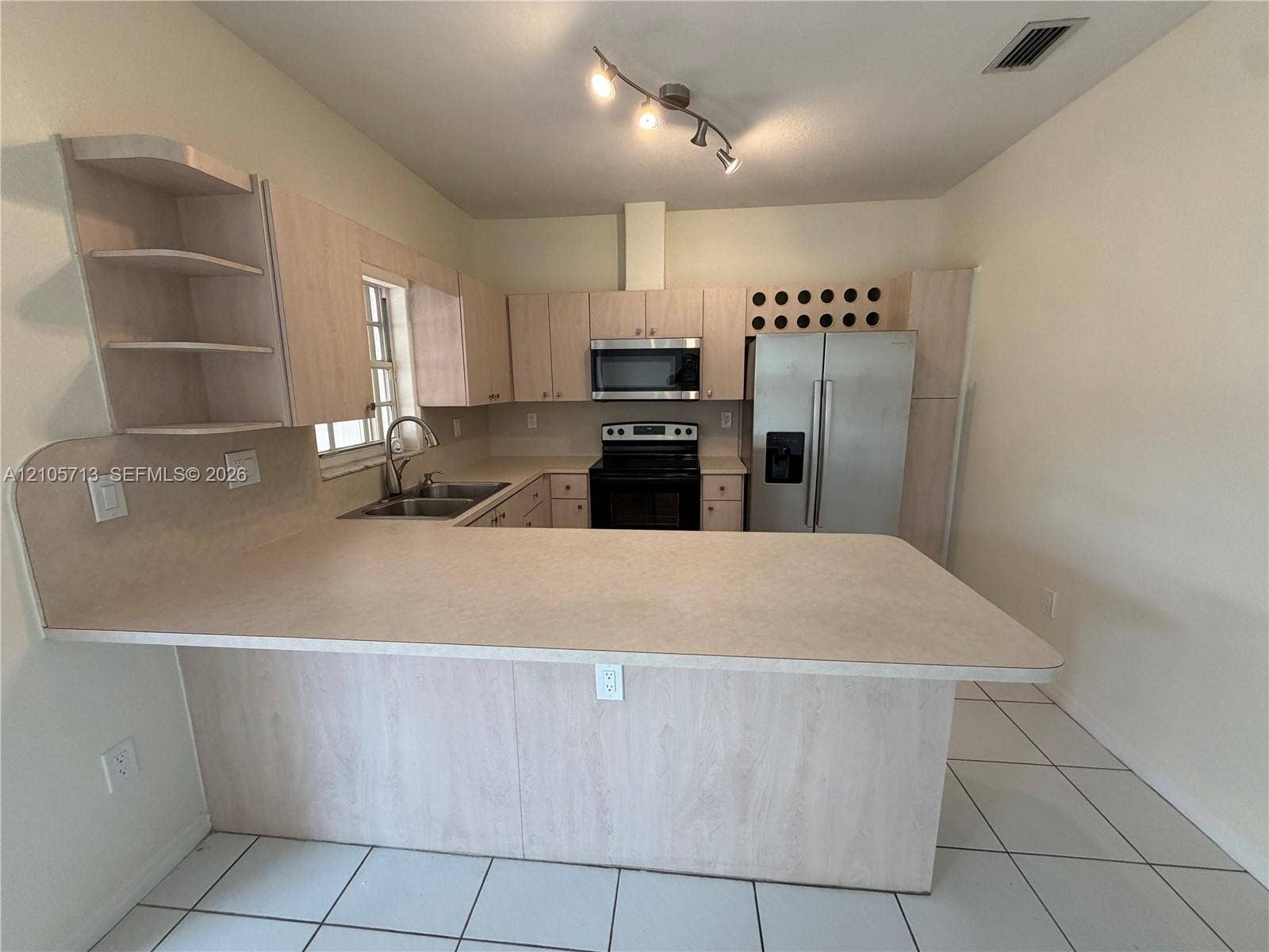 Kitchen featuring light-tone cabinetry, built-in wine storage, solid surface countertops, stainless steel appliances, and ceramic tile flooring