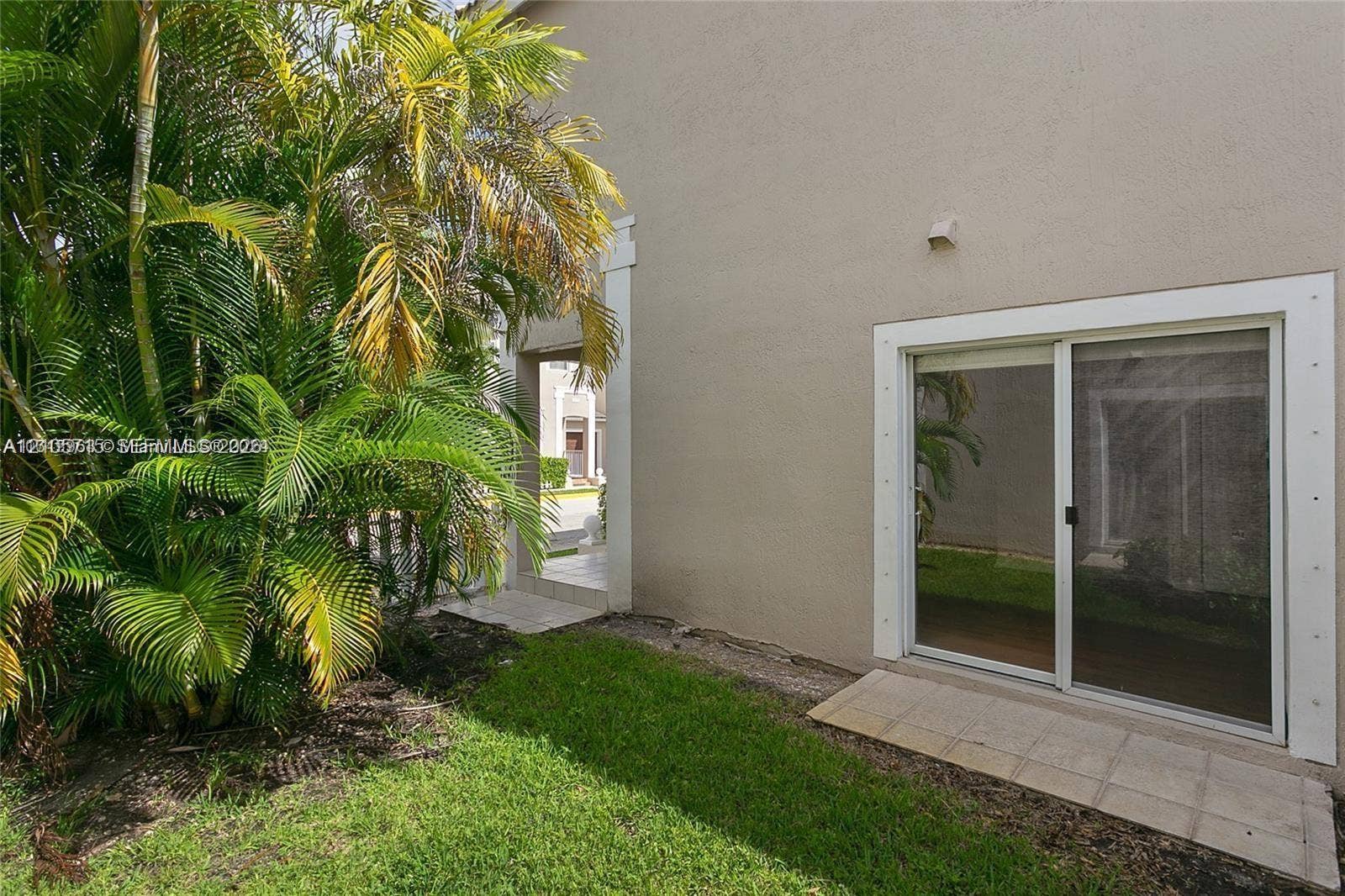 10524 NW 57th Court, Coral Springs, FL 33076 Stucco exterior featuring sliding glass doors with white trim, tile patio landing, and established palm landscaping
