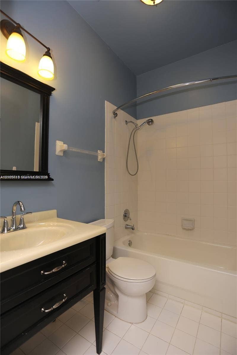 10524 NW 57th Court, Coral Springs, FL 33076 Bathroom featuring a black vanity with a molded countertop, a curved shower rod, a handheld showerhead, and a ceramic tile floor