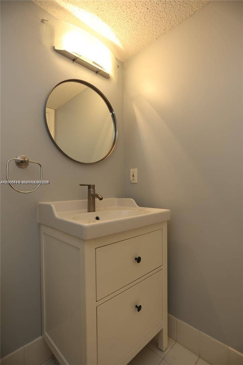 10524 NW 57th Court, Coral Springs, FL 33076 White vanity with two drawers, integrated porcelain basin, metallic finish faucet, round mirror, and wall-mounted light fixture