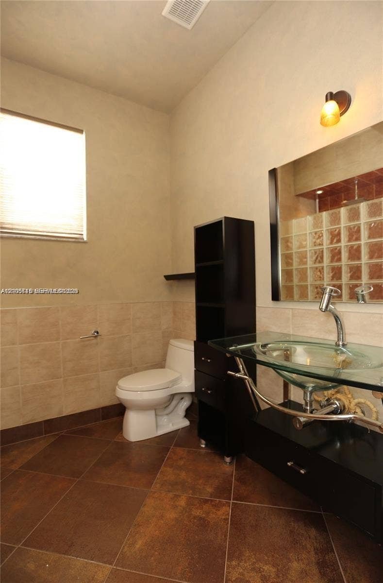 10524 NW 57th Court, Coral Springs, FL 33076 Bathroom featuring a glass vessel sink, dark cabinetry, ceramic tile flooring, and a glass block accent wall