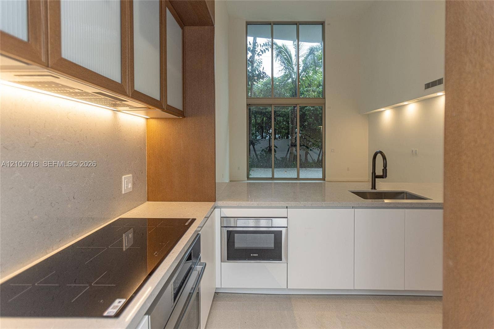 2200 Brickell Avenue, #GV16, Miami, FL 33129 Kitchen featuring custom wood-toned cabinetry with glass-paneled upper doors, stone countertops, a flat-surface induction cooktop, integrated stainless steel appliances, and floor-to-ceiling windows