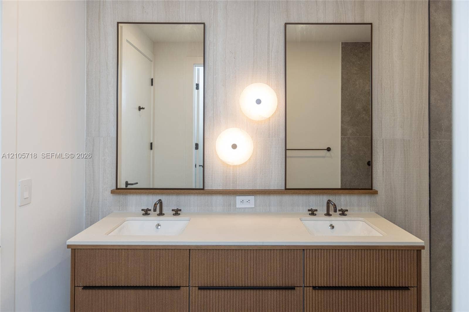 2200 Brickell Avenue, #GV16, Miami, FL 33129 Master bath Double vanity with a textured wood-finish cabinet, stone-finish countertop, dual rectangular undermount sinks, bronze-finish widespread faucets, and twin rectangular mirrors