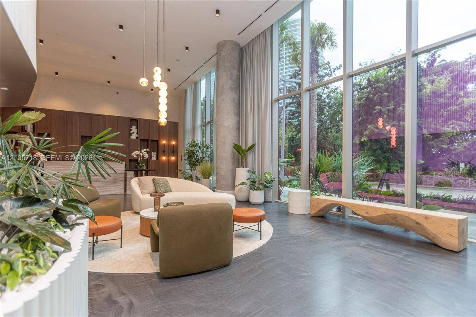 2200 Brickell Avenue, #GV16, Miami, FL 33129 Double-height floor-to-ceiling windows, dark stone flooring, exposed concrete structural column, recessed ceiling lighting, and built-in wood-veneer cabinetry