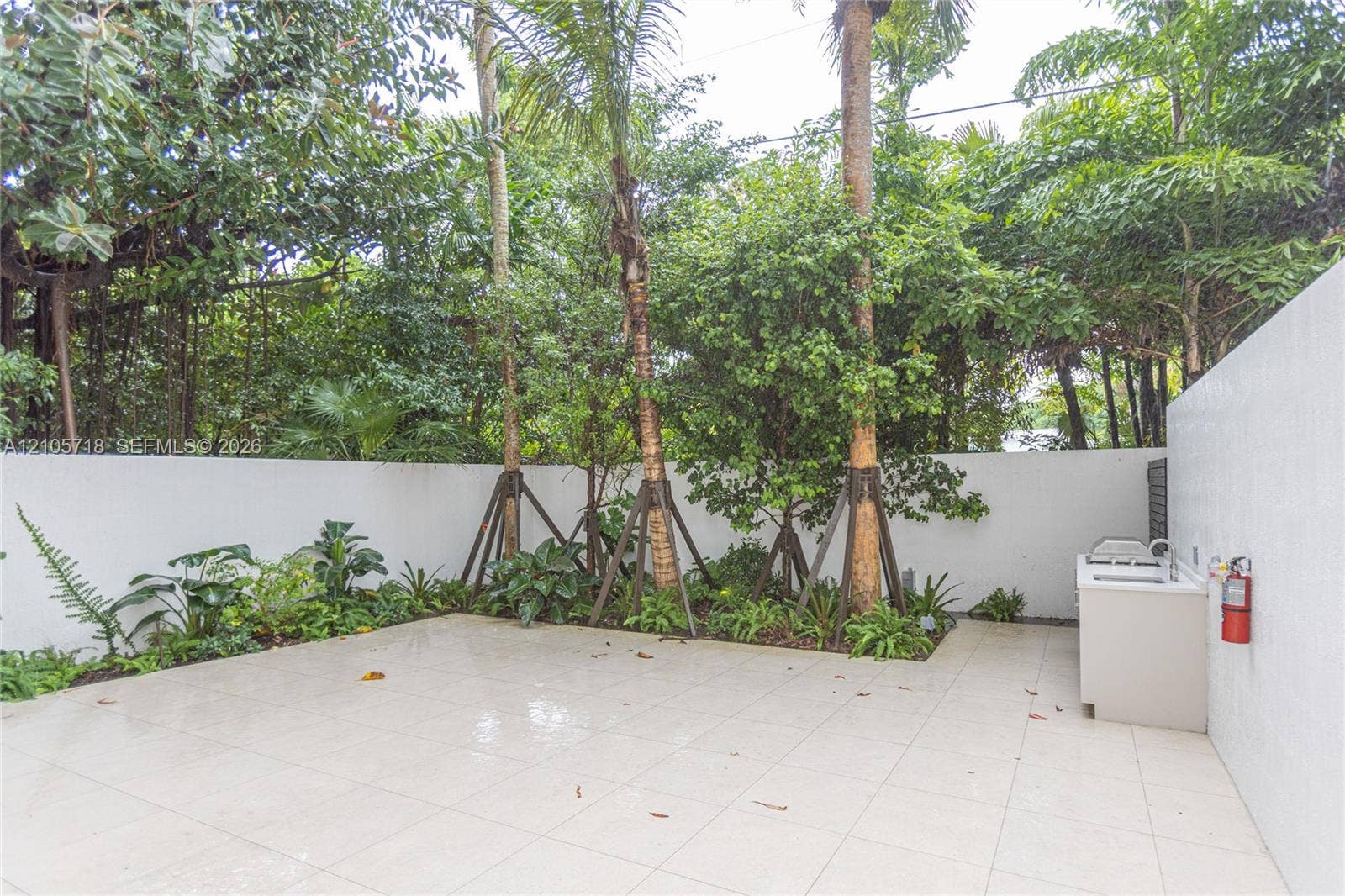 2200 Brickell Avenue, #GV16, Miami, FL 33129 Outdoor courtyard featuring large-format tile flooring, built-in masonry counter with sink, solid perimeter wall, and established landscaping with mature palm trees