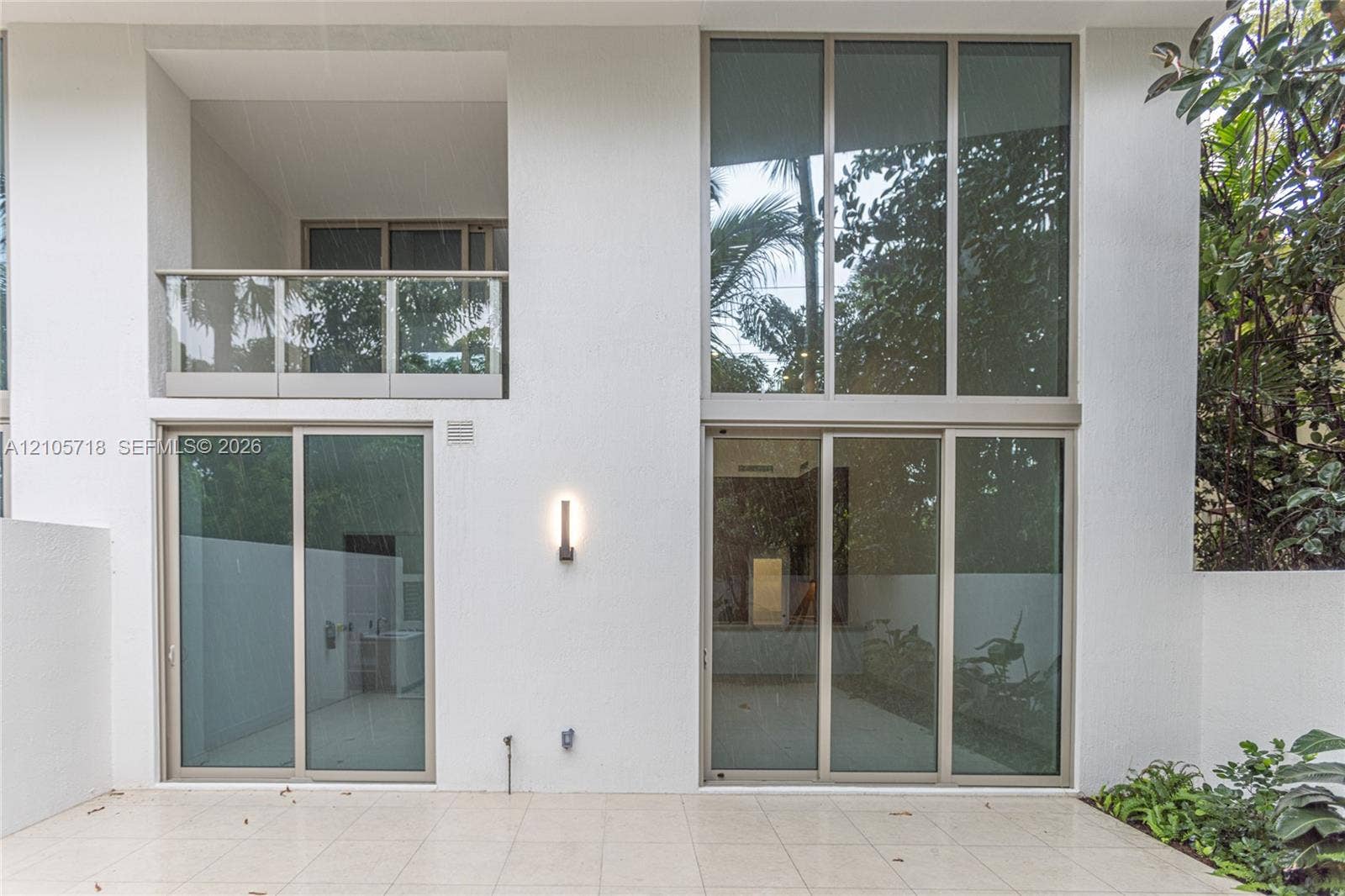 2200 Brickell Avenue, #GV16, Miami, FL 33129 Exterior elevation featuring expansive two-story floor-to-ceiling windows, a covered balcony with a glass railing, large-format tile patio flooring, and wall-mounted minimalist lighting