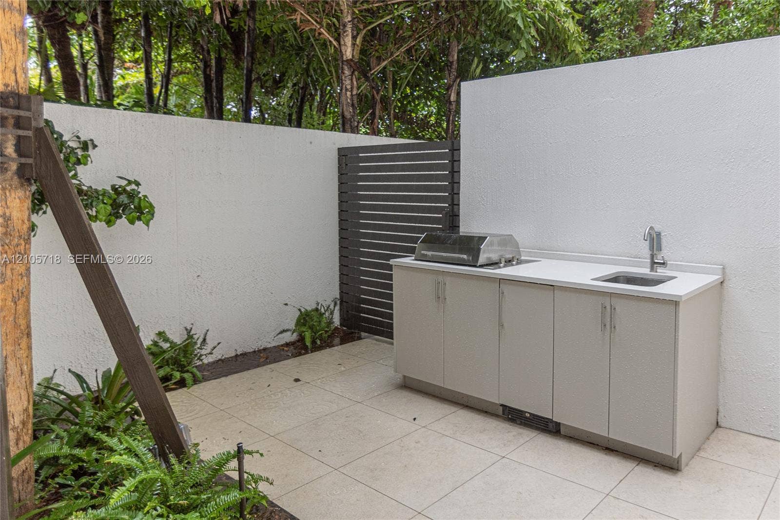 2200 Brickell Avenue, #GV16, Miami, FL 33129 Outdoor kitchen area featuring large-format tile flooring, a stone-finish countertop, stainless steel integrated grill, undermount sink, and privacy wall