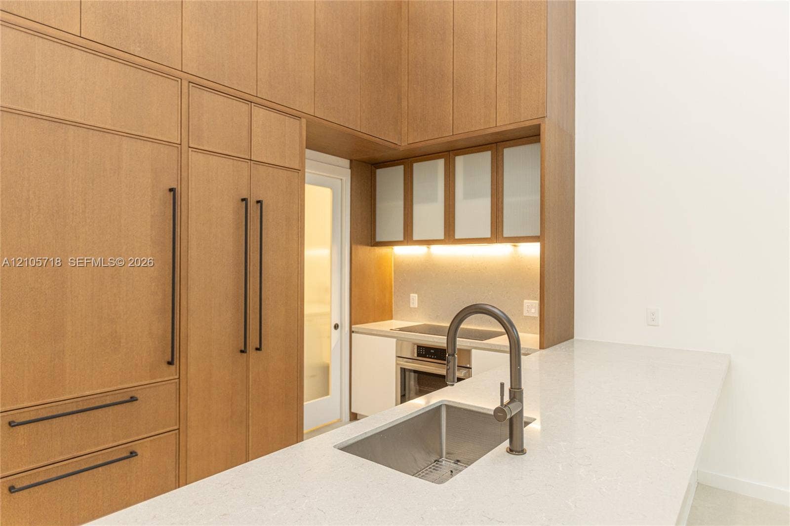 2200 Brickell Avenue, #GV16, Miami, FL 33129 Floor-to-ceiling wood-finish cabinetry, integrated refrigerator, stone countertop with waterfall edge, undermount stainless steel sink, and glass-paneled upper cabinets