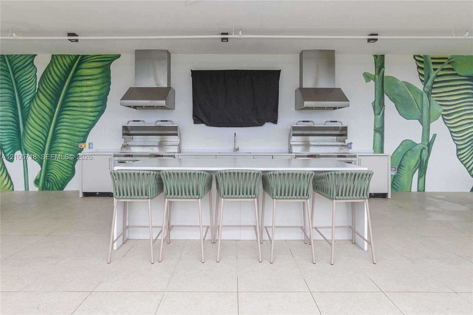 2200 Brickell Avenue, #GV16, Miami, FL 33129 Outdoor kitchen featuring dual stainless steel grills, matching stainless steel range hoods, a central prep island with white countertop, and large-scale botanical wall murals
