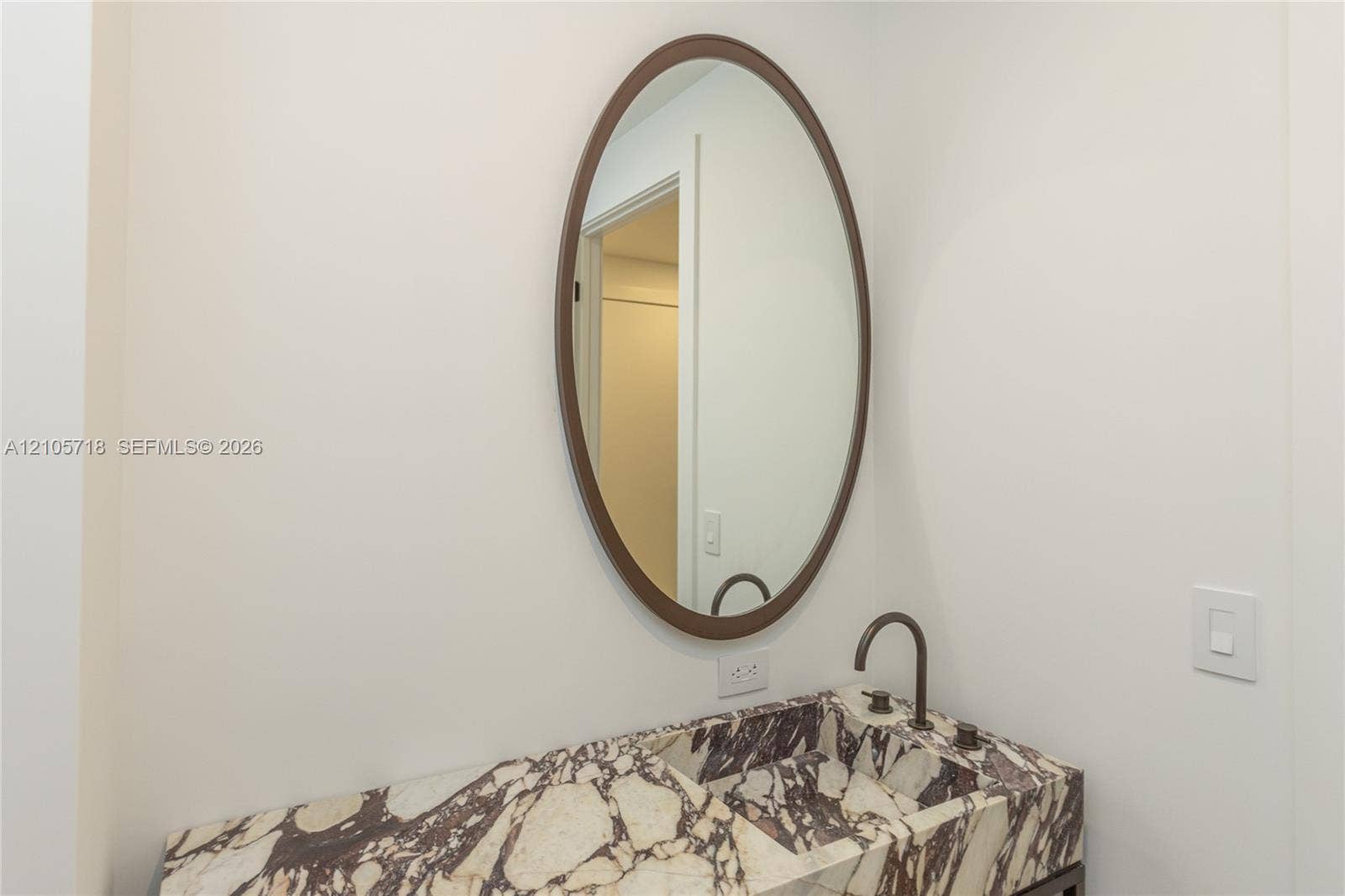 2200 Brickell Avenue, #GV16, Miami, FL 33129 Stone countertop with an integrated basin, oval wall-mounted mirror with a bronze-toned frame, and a bronze-toned gooseneck faucet