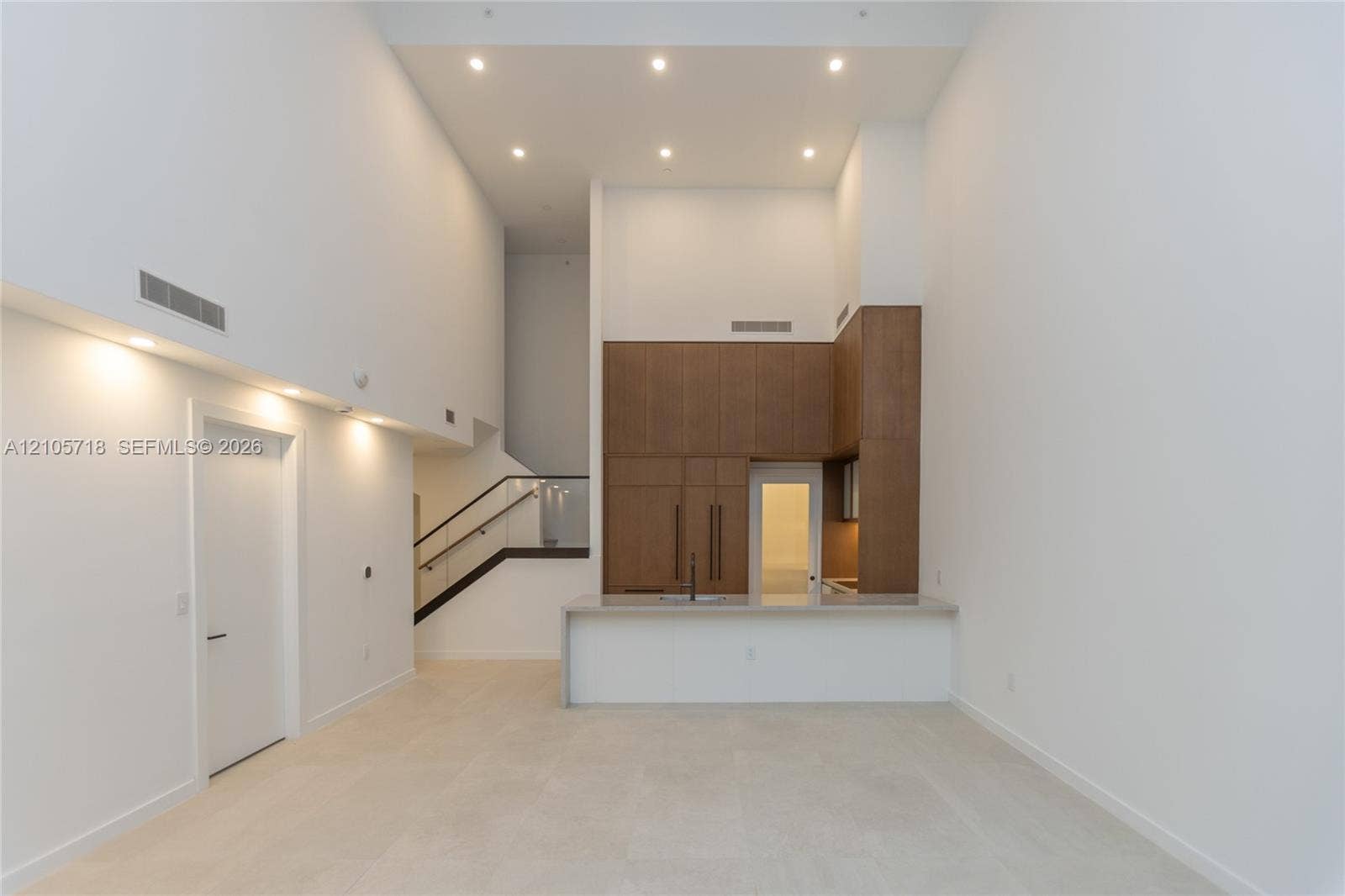 2200 Brickell Avenue, #GV16, Miami, FL 33129 Double-height ceilings featuring recessed lighting, full-height wood-finish cabinetry, stone-surfaced kitchen island, and metal railing staircase