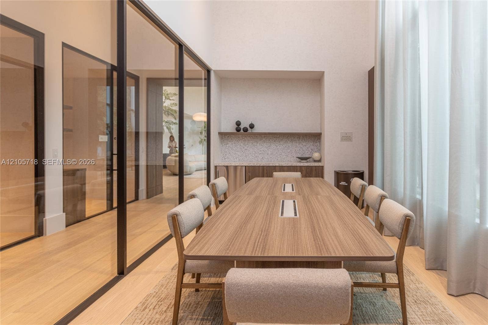 2200 Brickell Avenue, #GV16, Miami, FL 33129 High-ceilinged room featuring expansive glass wall partitions with black metal frames, integrated built-in cabinetry with stone-surface counters, and light-toned wood-finish flooring