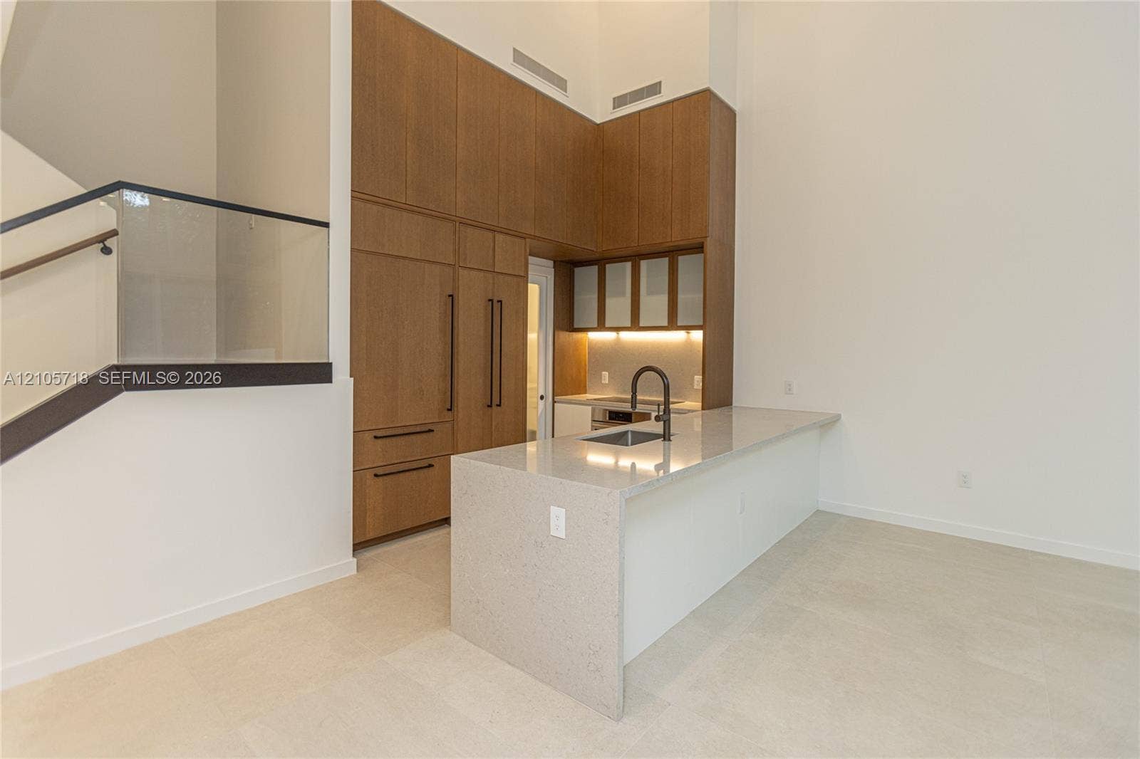2200 Brickell Avenue, #GV16, Miami, FL 33129 Kitchen featuring full-height wood-finish cabinetry, waterfall-edge stone countertop, undermount sink with matte black faucet, and glass staircase railing