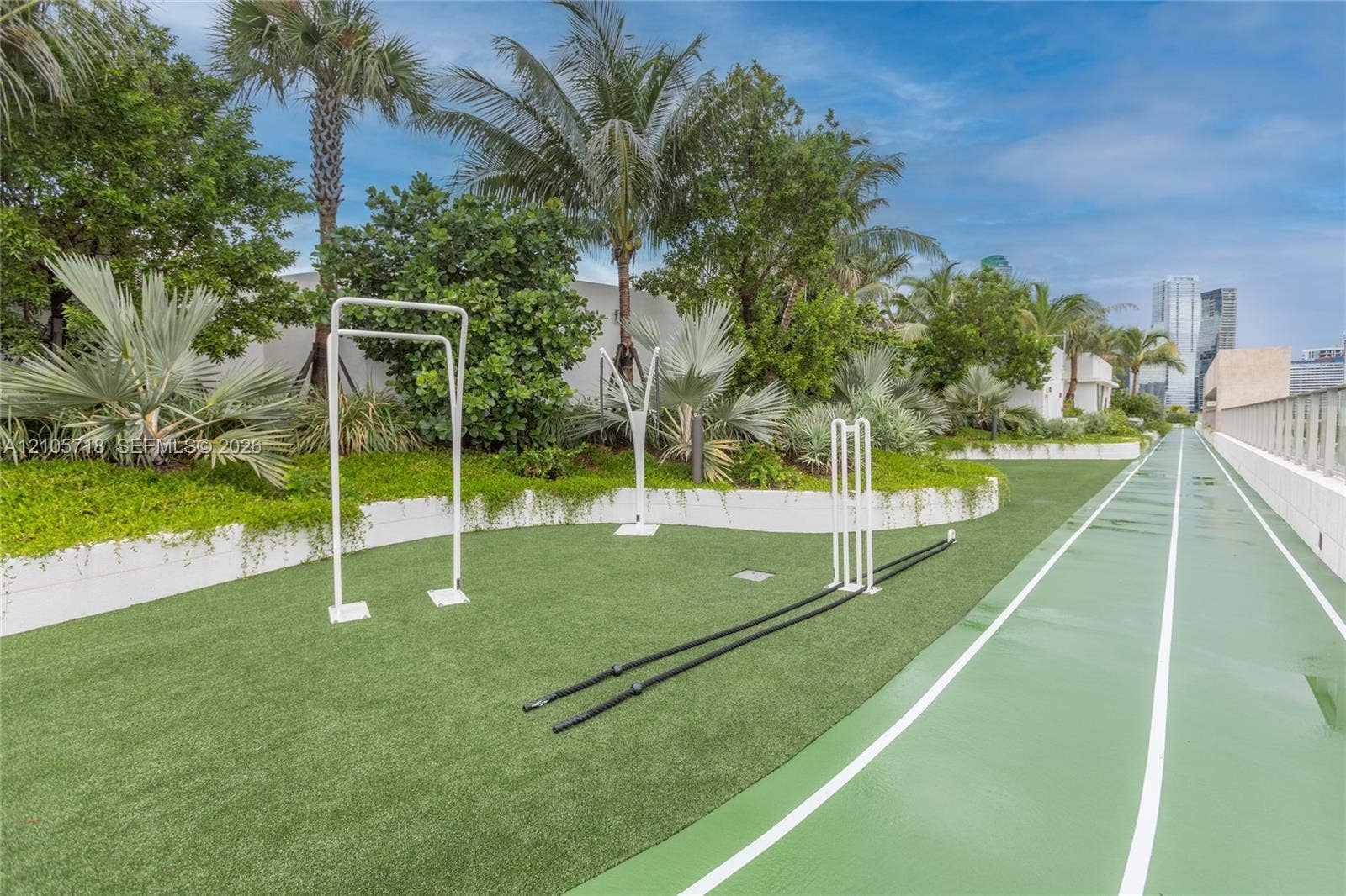 2200 Brickell Avenue, #GV16, Miami, FL 33129 Outdoor fitness area featuring a synthetic running track, multi-use exercise frames, manicured landscaping with mature palms, and tiered retaining walls