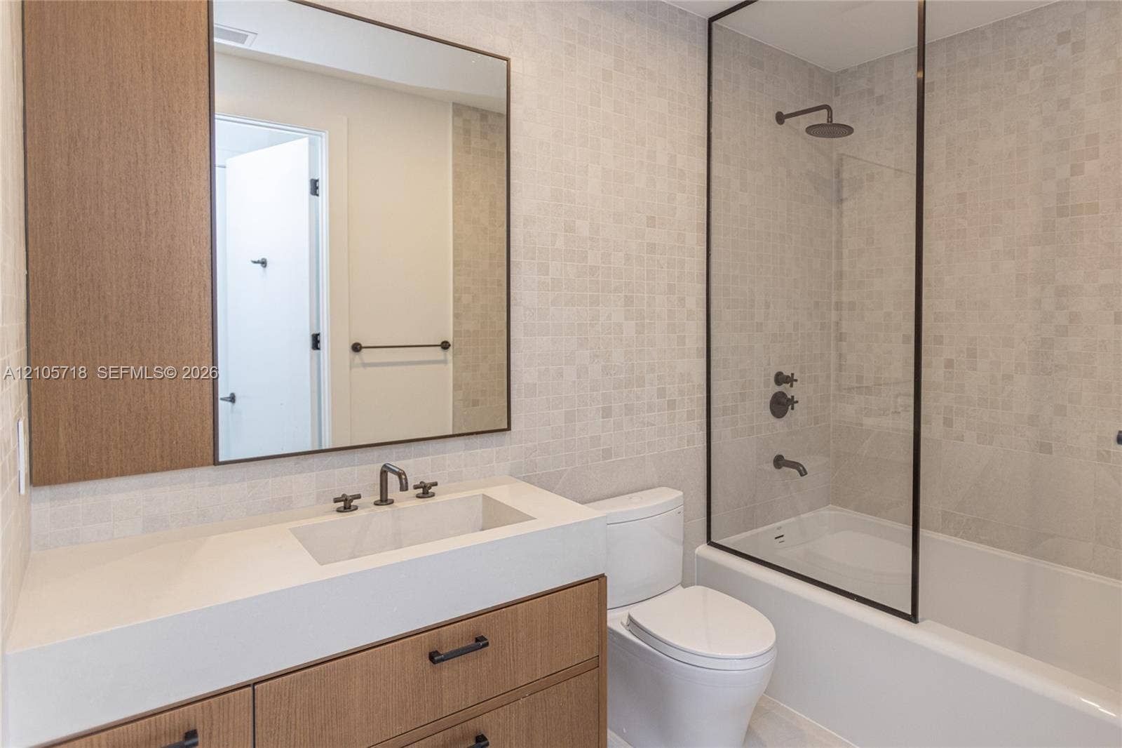 2200 Brickell Avenue, #GV16, Miami, FL 33129 Modern vanity with wood-finish cabinetry, integrated countertop with rectangular basin, matte black plumbing fixtures, glass-enclosed shower, and mosaic tile wall accents