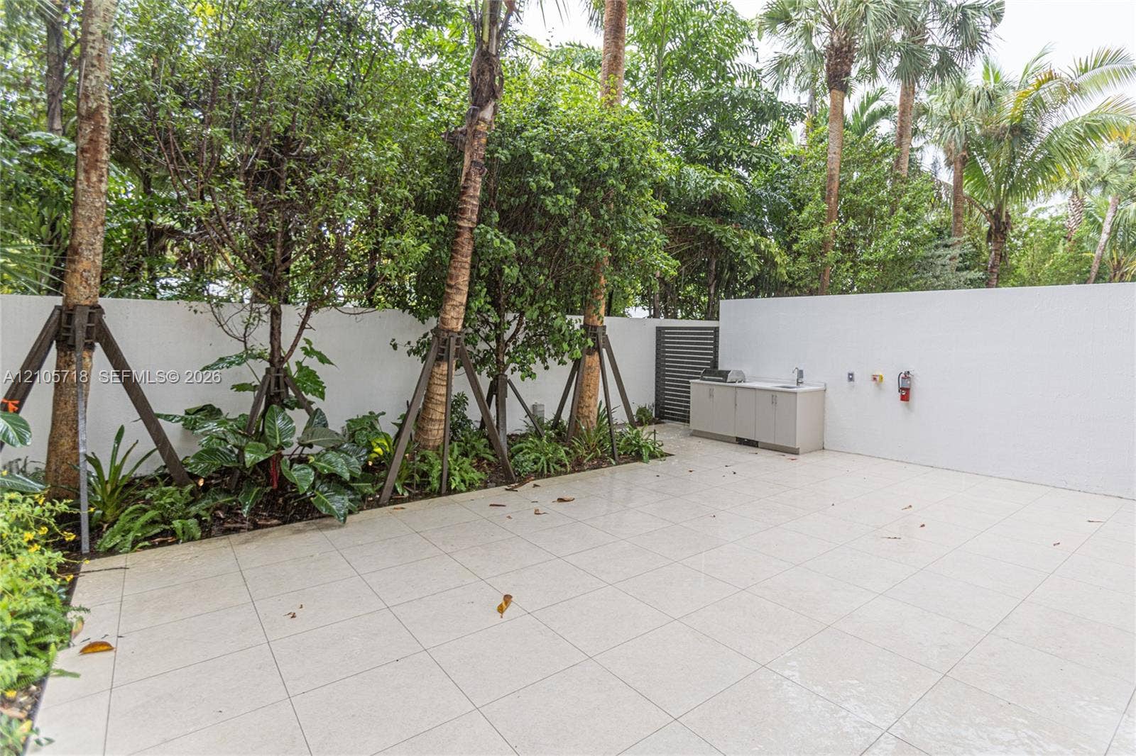 2200 Brickell Avenue, #GV16, Miami, FL 33129 Private outdoor patio featuring light-toned tile flooring, built-in cabinetry with a sink, stainless steel grill, solid privacy walls, and mature perimeter landscaping