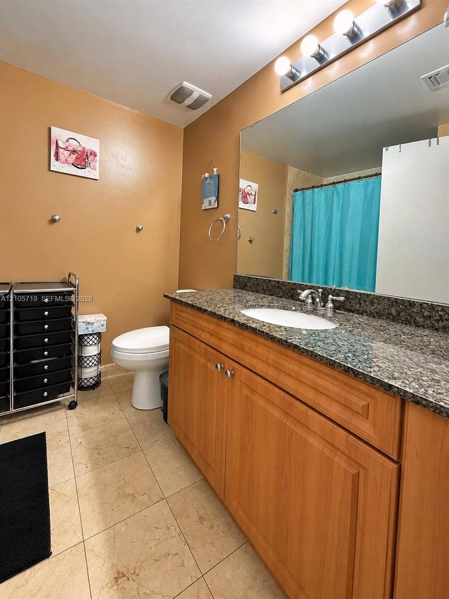 1 Glen Royal Parkway, #1510, Miami, FL 33125 Bathroom featuring a wood-finish vanity with a stone-composite countertop, undermount sink, expansive wall-mounted mirror, and tile flooring