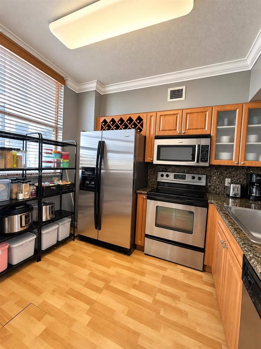 1 Glen Royal Parkway, #1510, Miami, FL 33125 Kitchen featuring wood-finish cabinetry, natural stone countertops, built-in wine storage, stainless steel appliances, and crown molding