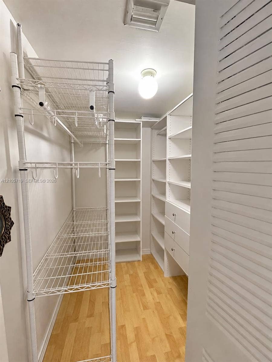 1 Glen Royal Parkway, #1510, Miami, FL 33125 Walk-in closet featuring wood-finish flooring, built-in floor-to-ceiling shelving, integrated drawer units, and tiered metal wire racking