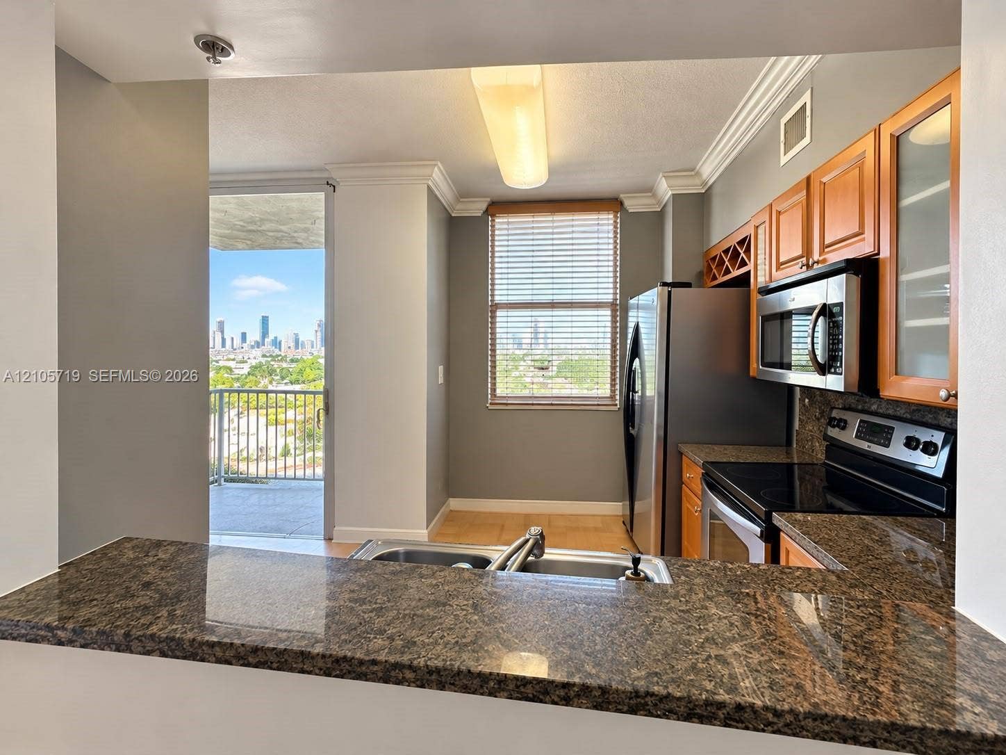 1 Glen Royal Parkway, #1510, Miami, FL 33125 Kitchen featuring a granite countertop peninsula, natural wood cabinetry with glass-front display panels, stainless steel built-in microwave, and crown molding