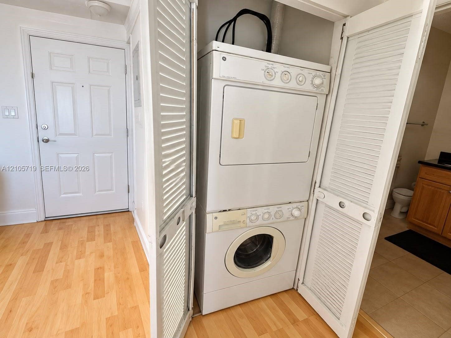 1 Glen Royal Parkway, #1510, Miami, FL 33125 Stacked laundry unit housed in a louvered-door closet featuring wood-finish flooring and a multi-panel interior door