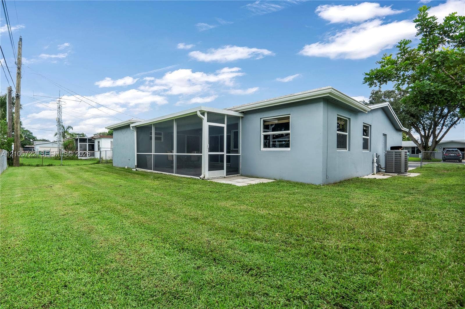8953 SW 53rd Street, Cooper City, FL 33328 Rear exterior featuring a stucco facade, an attached screened-in patio, and an expansive lawn