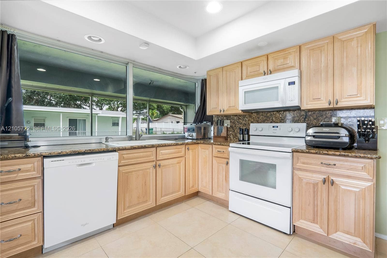 8953 SW 53rd Street, Cooper City, FL 33328 Kitchen featuring light-finish cabinetry, stone-texture countertops, large horizontal windows, tile flooring, and integrated white appliances