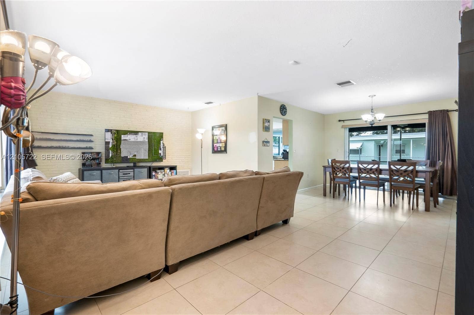 8953 SW 53rd Street, Cooper City, FL 33328 Open-concept main living area featuring light-toned tile flooring, a painted brick accent wall, and a large sliding glass door providing natural light