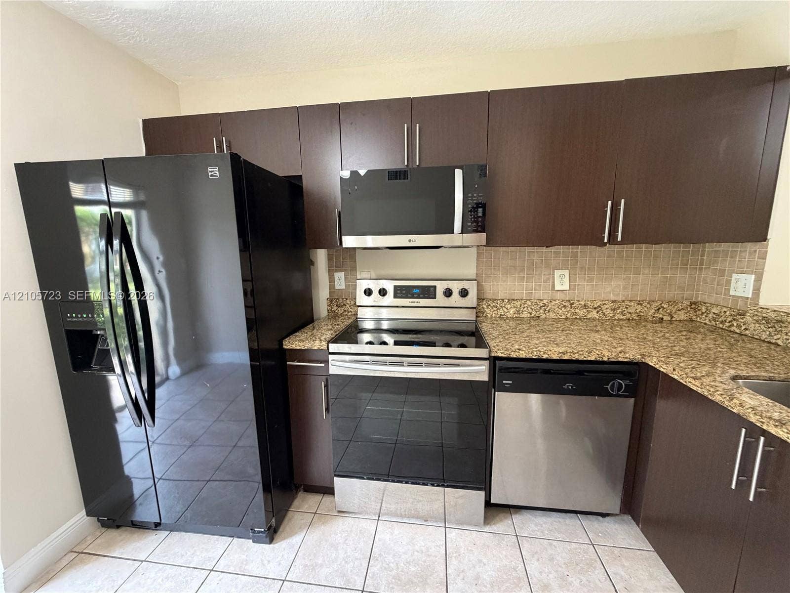 4785 SW 62nd Avenue, #102, Davie, Davie, FL 33314 Kitchen featuring dark-finish cabinetry, stone-style countertops, mosaic tile backsplash, and a suite of stainless steel and black appliances, including a built-in microwave and dishwasher