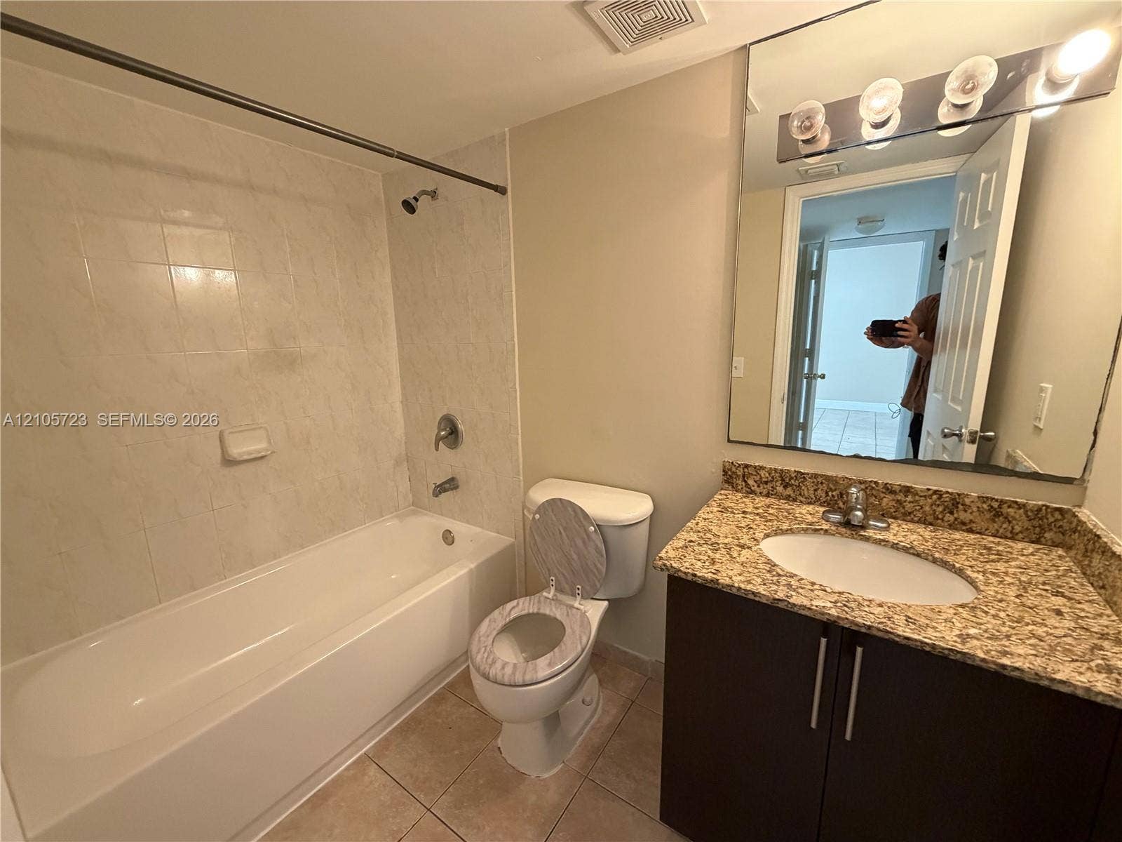 4785 SW 62nd Avenue, #102, Davie, Davie, FL 33314 Bathroom featuring a stone-surface vanity with an integrated oval sink, dark cabinetry, large wall-mounted mirror, four-bulb light fixture, and a tile-surround bathtub