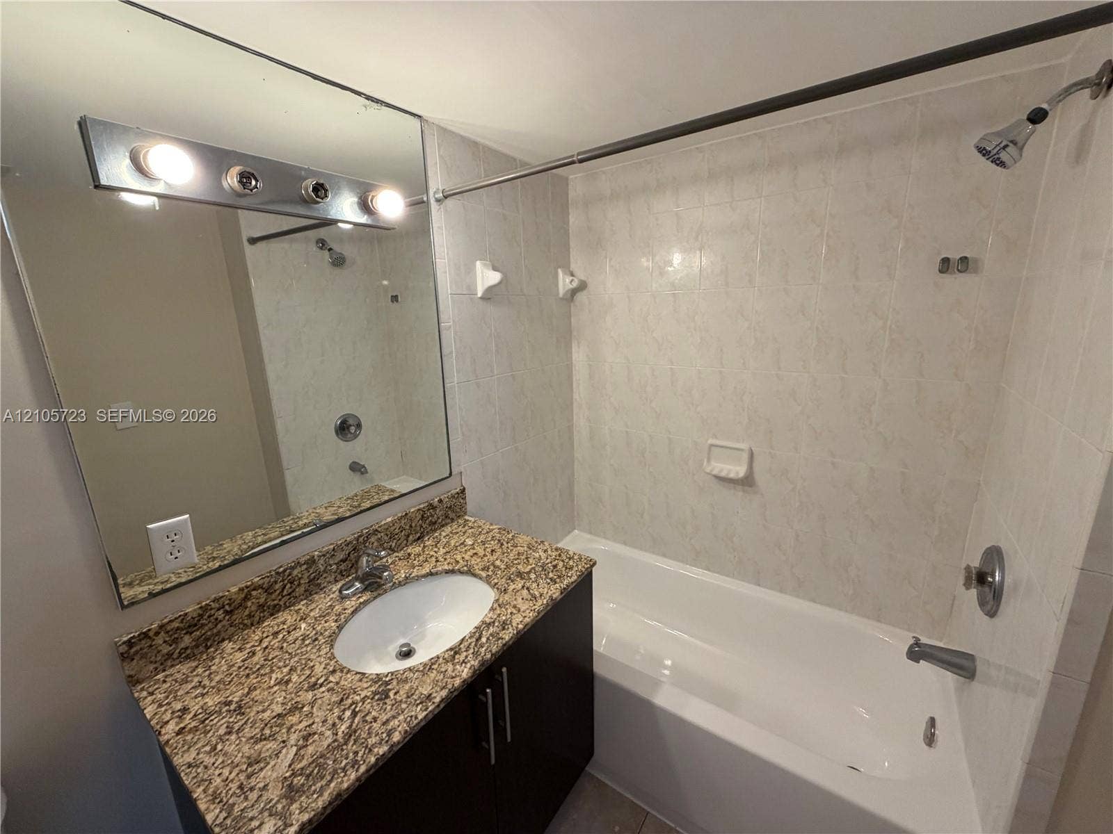 4785 SW 62nd Avenue, #102, Davie, Davie, FL 33314 Bathroom featuring a vanity with stone-finish countertop, undermount sink, full-width mirror, tile-surround bathtub, and polished metal fixtures