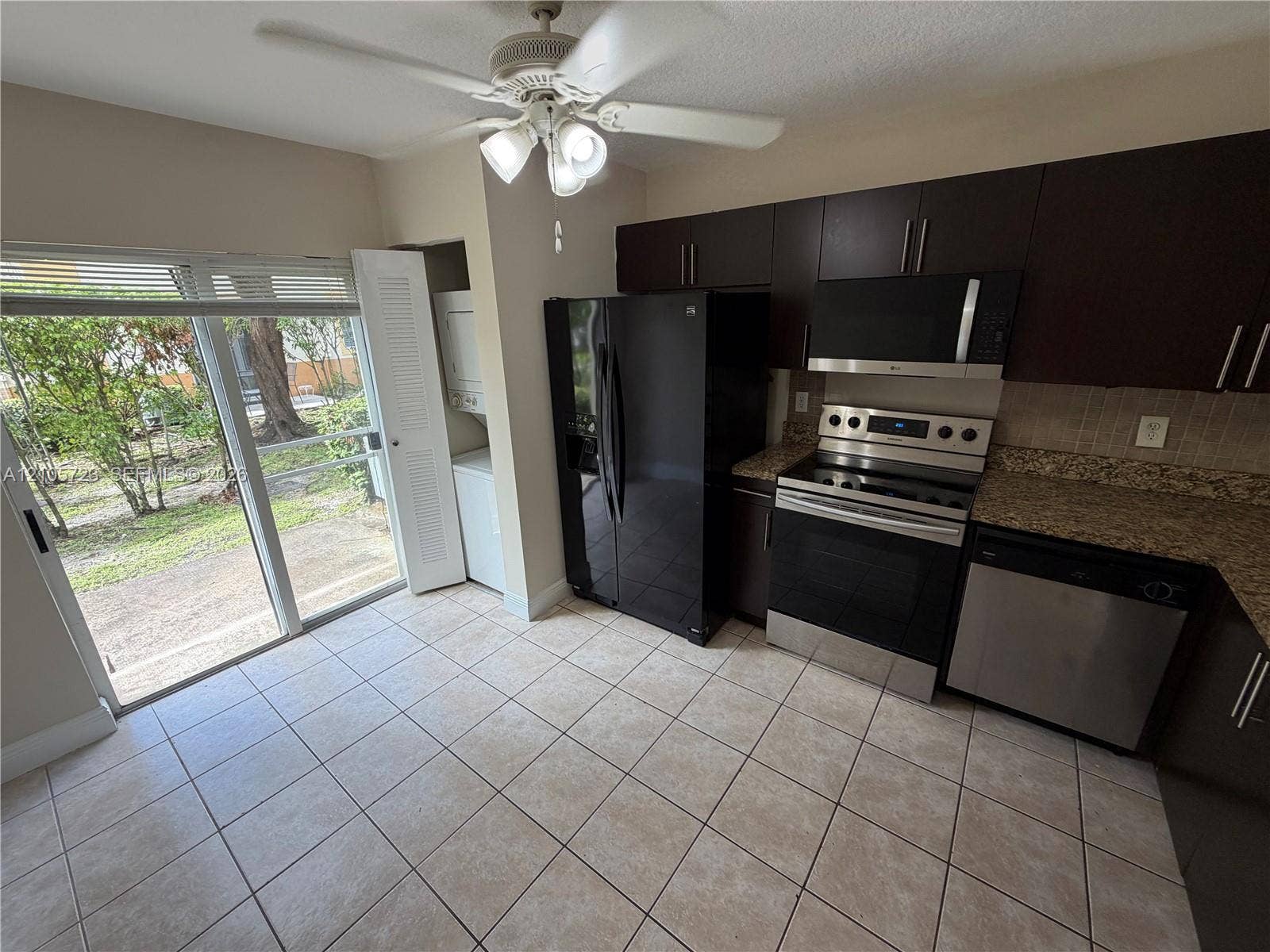 4785 SW 62nd Avenue, #102, Davie, Davie, FL 33314 Kitchen featuring dark wood-finish cabinetry, stone-style countertops, stainless steel appliances, tile flooring, and a sliding glass door