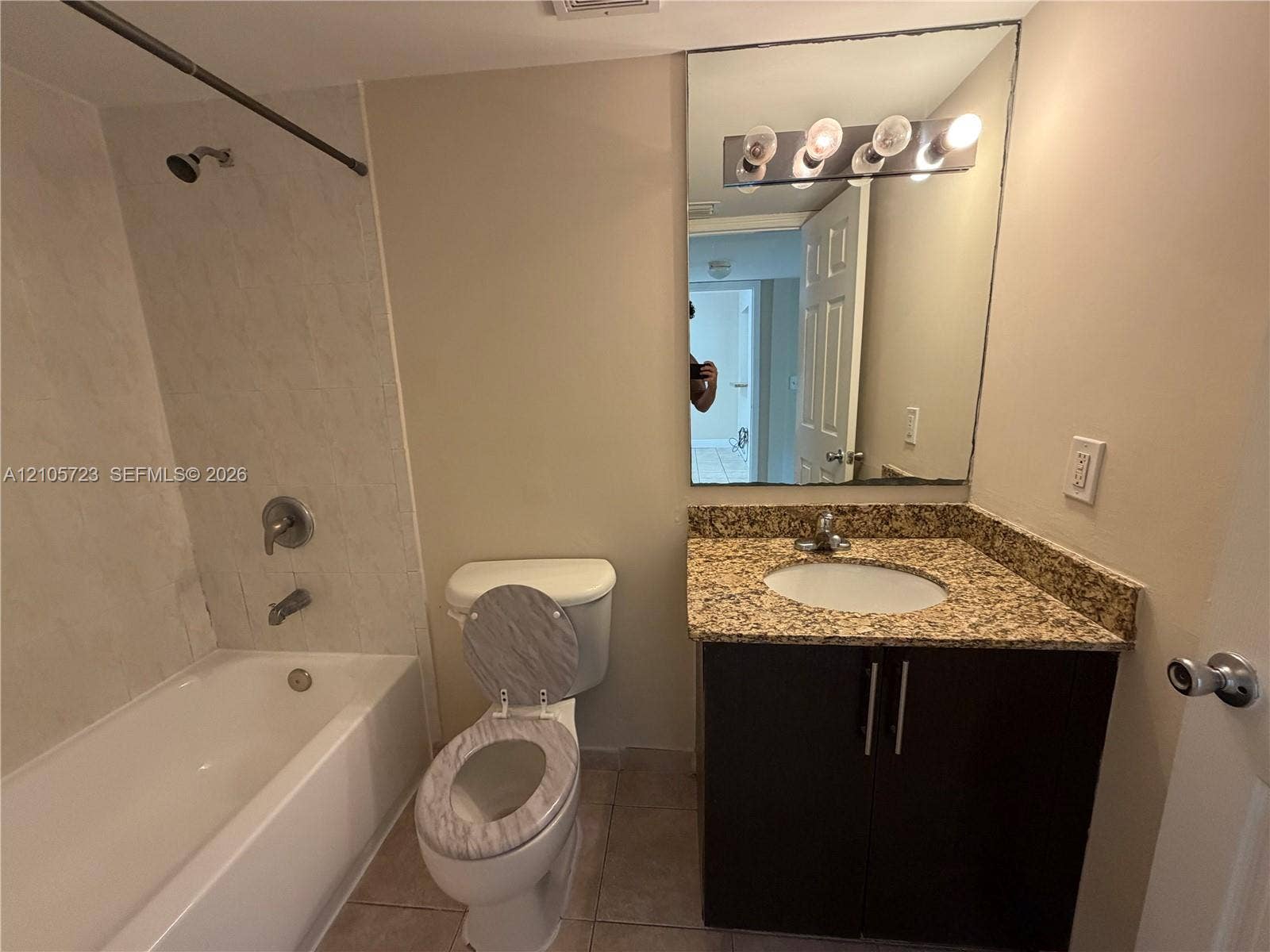 4785 SW 62nd Avenue, #102, Davie, Davie, FL 33314 Bathroom featuring a vanity with stone-finish countertop, dark wood-tone cabinetry, a large wall-mounted mirror with multi-bulb light fixture, and a tile-surround shower and tub combination